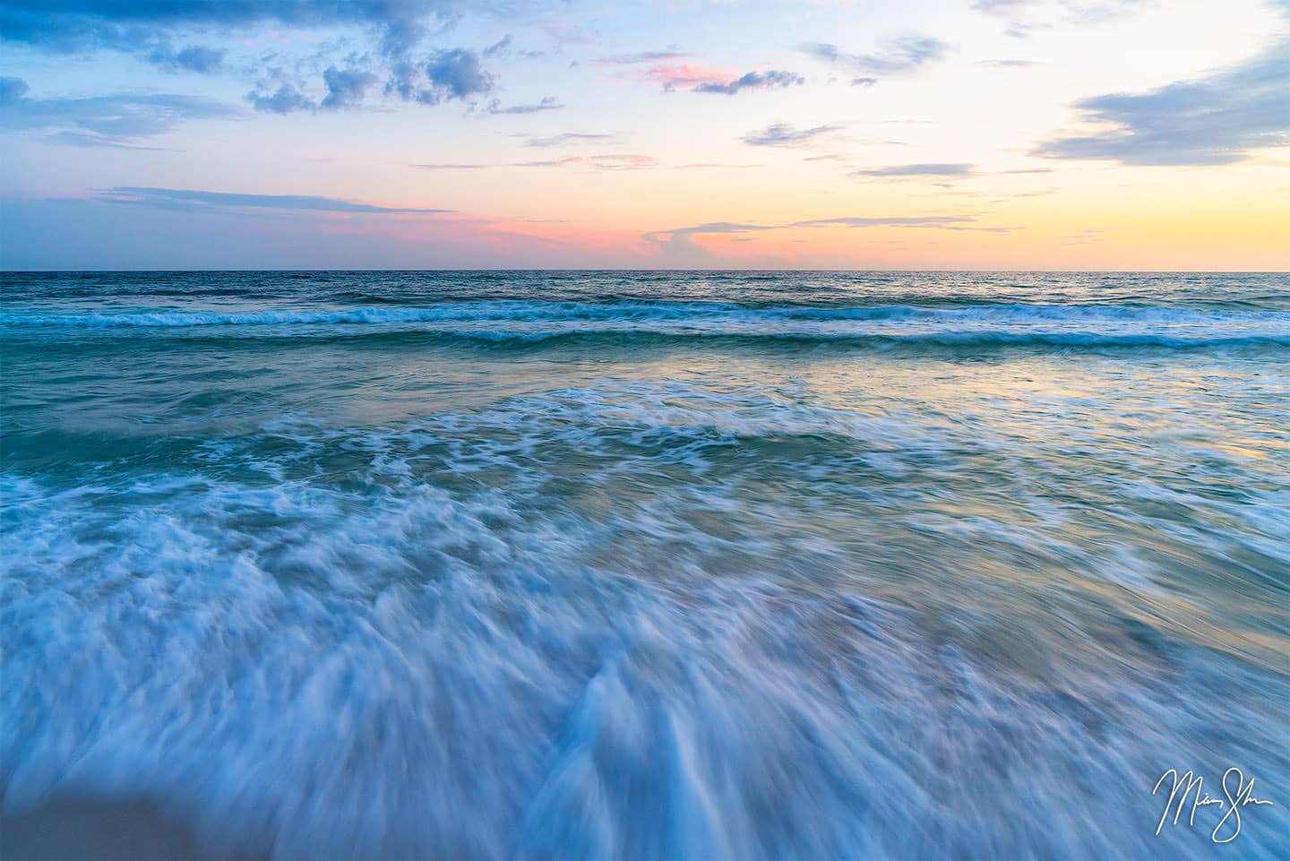 Clear water rushes the white sand beach at Destin as a pastel sunset lights up in the sky