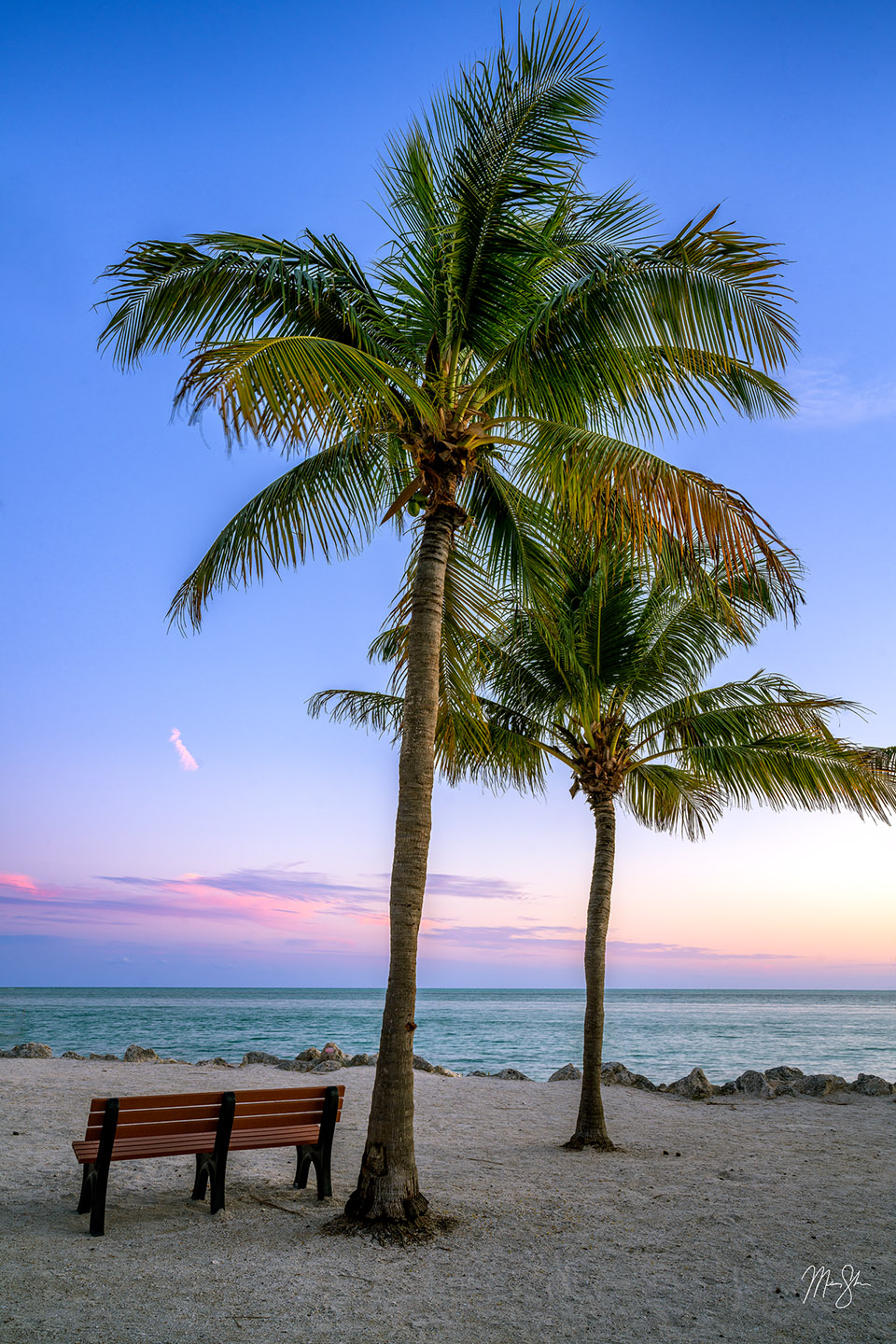 Two beautiful palm trees and a park bench face the ocean just after sunset on this small section of coastline in Marathon of the Florida Keys. Marathon is one of the last islands before Key West and the end of the road. I loved this little park area with palm trees and benches to relax and watch the sunset.