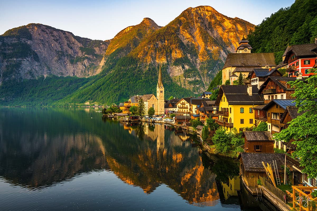 Featured: Hallstatt Sunrise | Alpenglow hits the mountains behind the famous town of Hallstatt in Austria as the buildings reflect in the lake below.